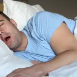 Mężczyzna śpi na boku, z otwartymi ustami, co sugeruje ślinotok.