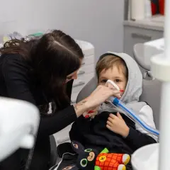 Dziecko w masce gazowej u dentysty, obok kobieta. Może to być reakcja na powikłania po znieczuleniu u dentysty.