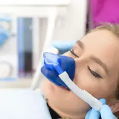 Kobieta z maską do sedacji na twarzy, przygotowana do zabiegu.