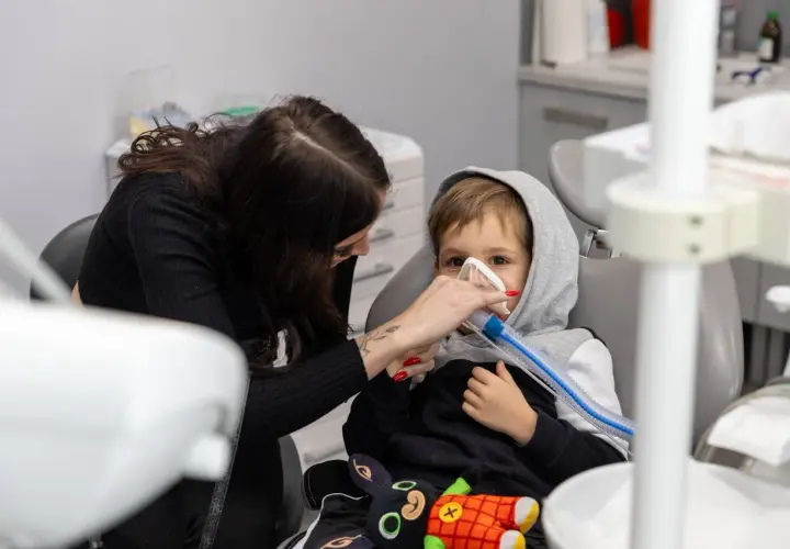 Dziecko w masce gazowej u dentysty, obok kobieta. Może to być reakcja na powikłania po znieczuleniu u dentysty.