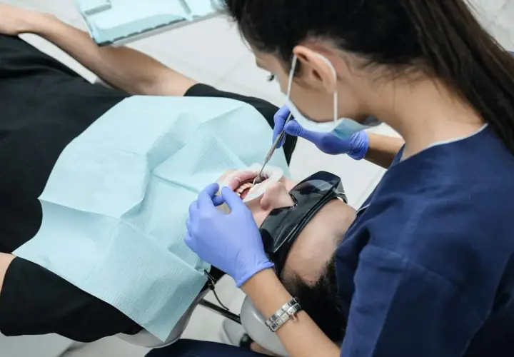 Dentystka w rękawiczkach zakłada pacjentowi na zęby materiał, być może formokrezol, do leczenia kanałowego.