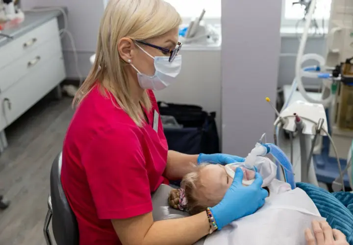 Dentystka w masce zakłada dziecku maskę znieczulającą. Obserwacja objawów uczulenia na znieczulenie u dentysty jest kluczowa.