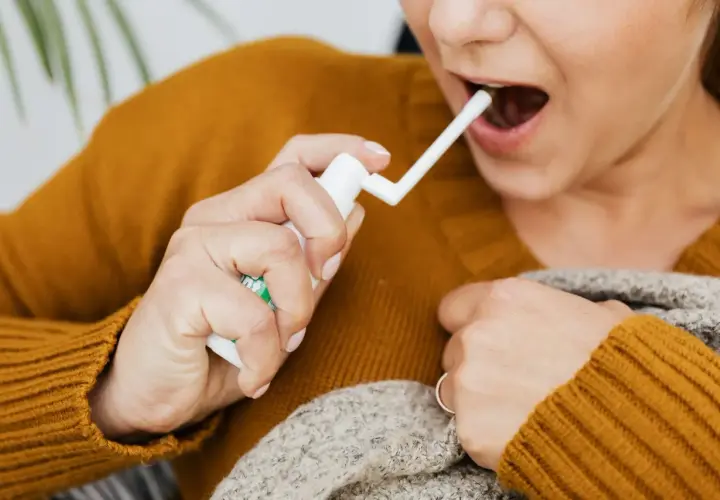 Kobieta aplikuje spray do gardła, łagodząc ból związany z aftami na migdałach. Zdjęcia pokazują jej dłoń z aplikatorem.