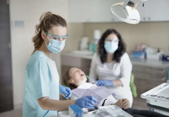 Dentystka w masce i okularach ochronnych wykonuje przegląd stomatologiczny pacjentki.
