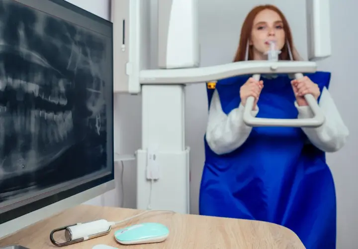 RTG zębów podczas ciąży jest bezpieczne. Kobieta w fartuchu ochronnym podchodzi do aparatu RTG.