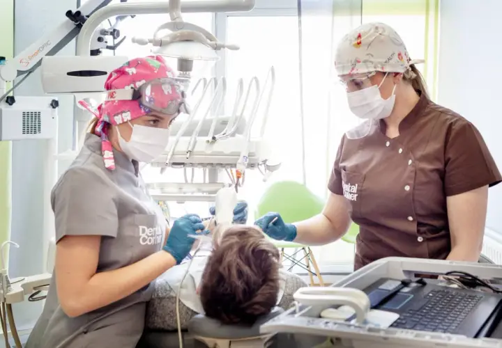 Dwie dentystki w maskach i okularach pracują przy pacjencie. Jedna z nich trzyma narzędzie, druga monitoruje. Szybkie bicie serca po znieczuleniu u dentysty to częsty objaw.