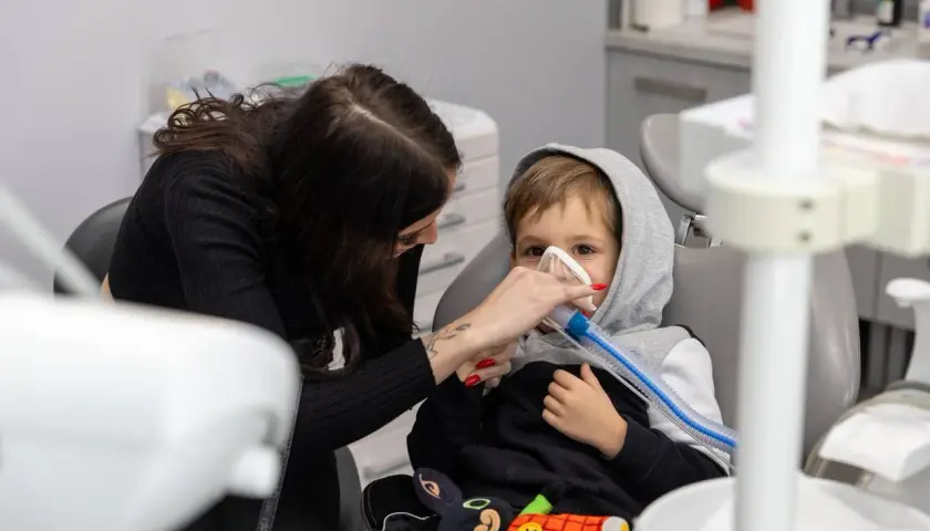 Dziecko w masce gazowej u dentysty, obok kobieta. Może to być reakcja na powikłania po znieczuleniu u dentysty.