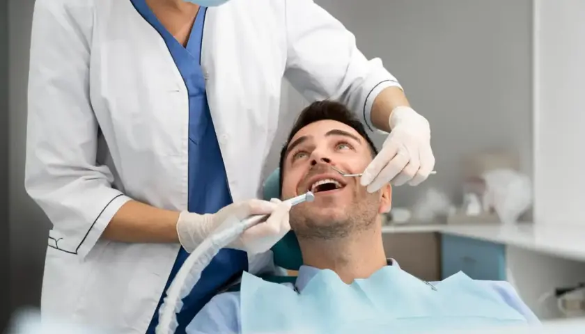 Pacjent uśmiecha się, gdy dentysta wykonuje zabieg. **Sedacja u dentysty** sprawia, że wizyta jest komfortowa i bezstresowa.