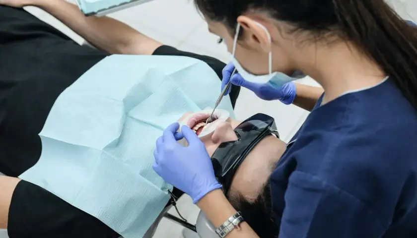 Dentystka w rękawiczkach zakłada pacjentowi na zęby materiał, być może formokrezol, do leczenia kanałowego.
