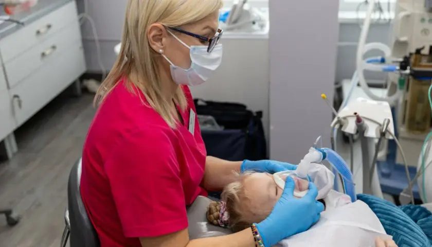 Dentystka w masce zakłada dziecku maskę znieczulającą. Obserwacja objawów uczulenia na znieczulenie u dentysty jest kluczowa.
