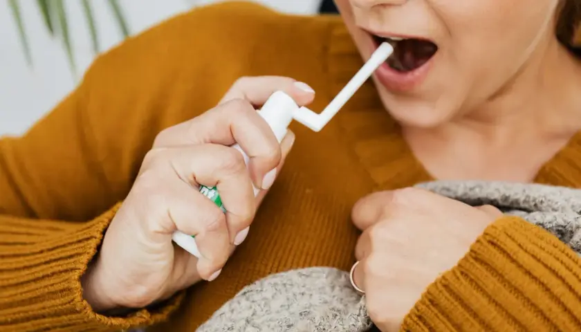 Kobieta aplikuje spray do gardła, łagodząc ból związany z aftami na migdałach. Zdjęcia pokazują jej dłoń z aplikatorem.