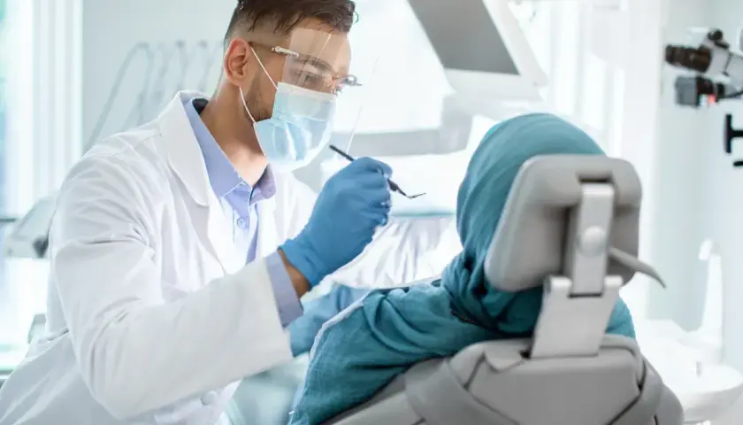 Lekarz stomatolog w masce i fartuchu bada pacjentkę w chuście. Nawet przy dentofobii, troska i profesjonalizm mogą pomóc.