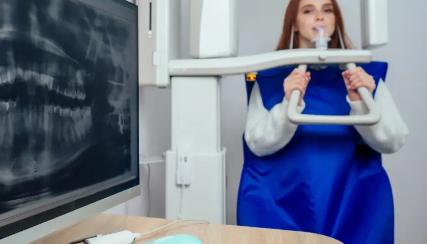RTG zębów podczas ciąży jest bezpieczne. Kobieta w fartuchu ochronnym podchodzi do aparatu RTG.