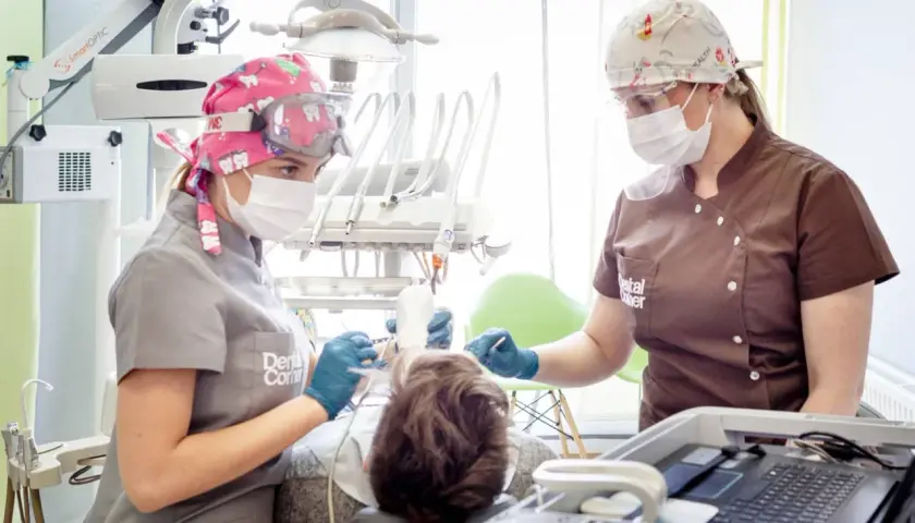Dwie dentystki w maskach i okularach pracują przy pacjencie. Jedna z nich trzyma narzędzie, druga monitoruje. Szybkie bicie serca po znieczuleniu u dentysty to częsty objaw.