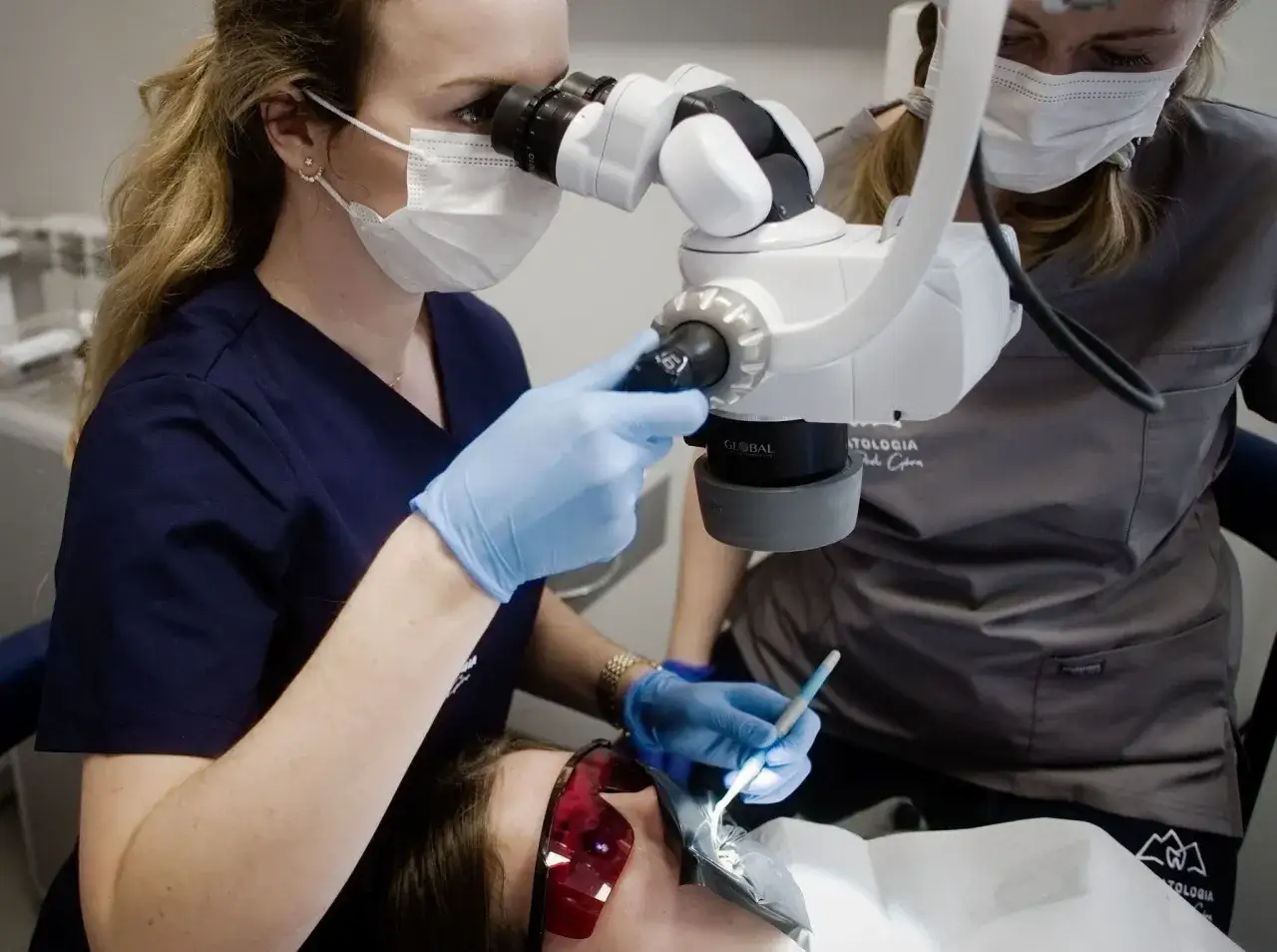 Dentystka z lupą stomatologiczną precyzyjnie zakłada domową plombę do zęba pacjentce.