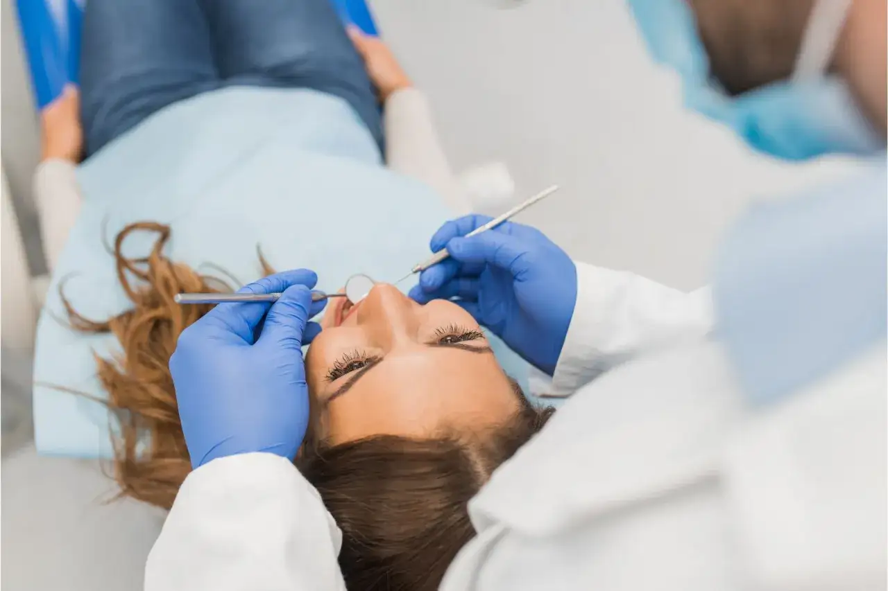 Dentysta w niebieskich rękawiczkach wykonuje zabieg stripping zębów u pacjentki leżącej na fotelu.
