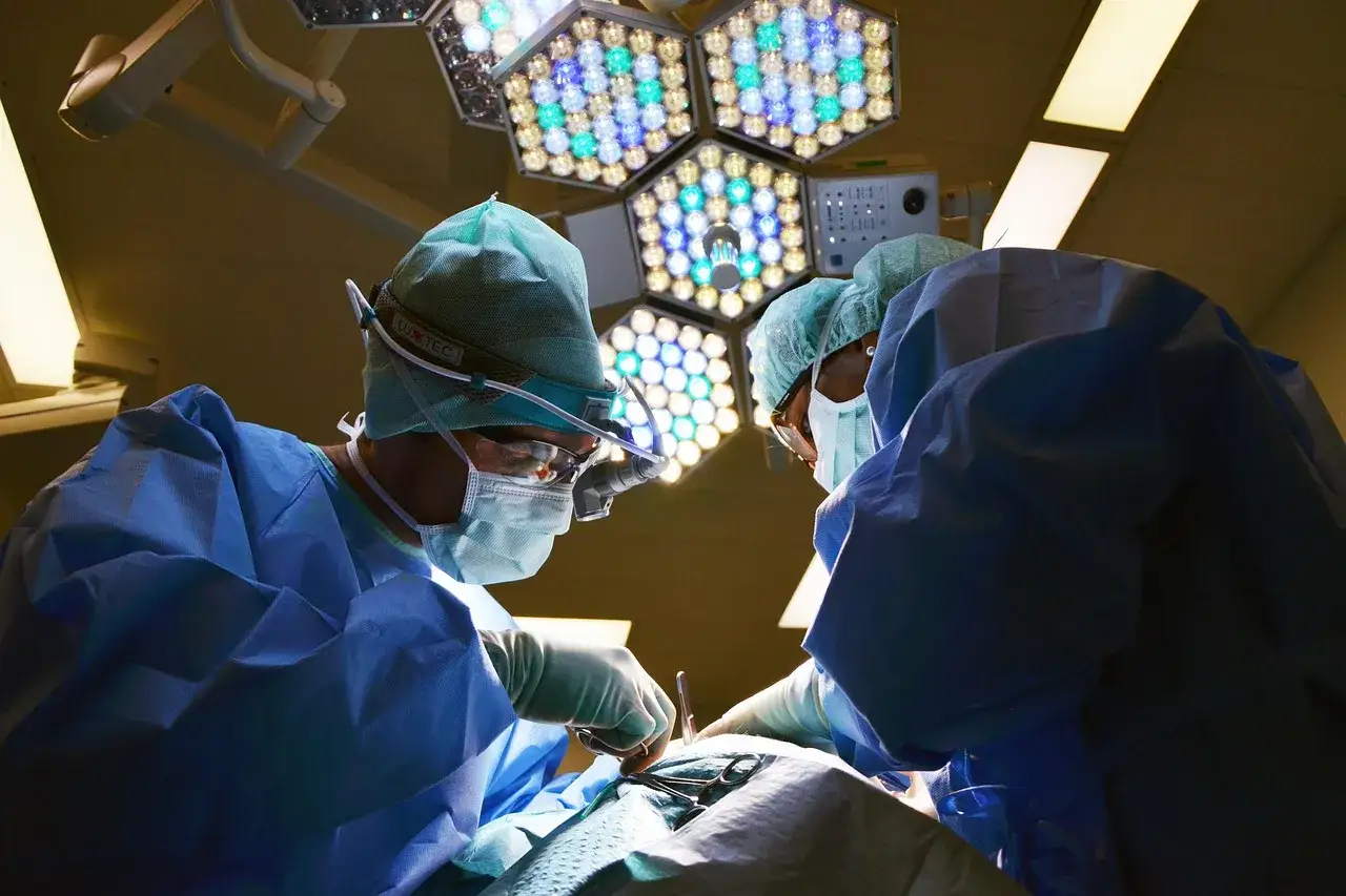 Chirurdzy w sterylnych strojach, pod jasnym światłem lampy operacyjnej, pracują nad pacjentem. Narkoza skutki uboczne to ryzyko, ale dzięki nim możliwe są ratujące życie zabiegi.