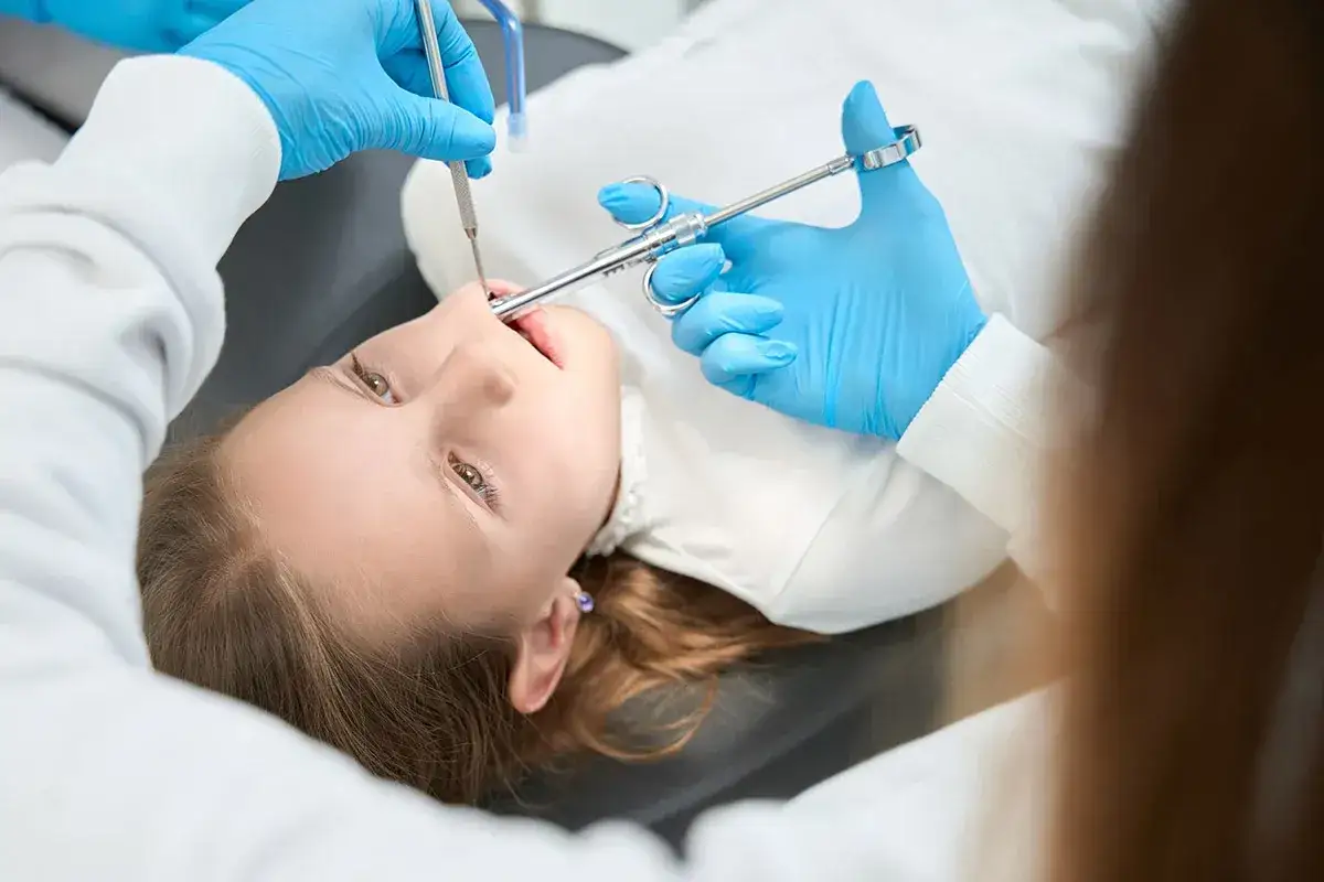 Dziecko uśmiecha się, gdy dentysta wykonuje znieczulenie nasiękowe.